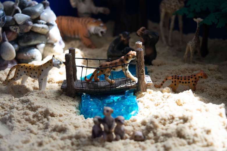 Cougar toys walking across a bridge in a sand tray