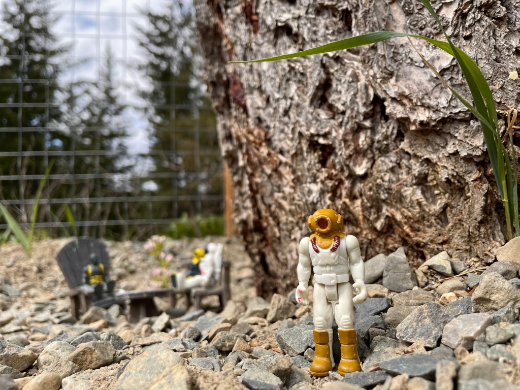 Toy standing by themselves in front of a tree with other toys sitting together in the background