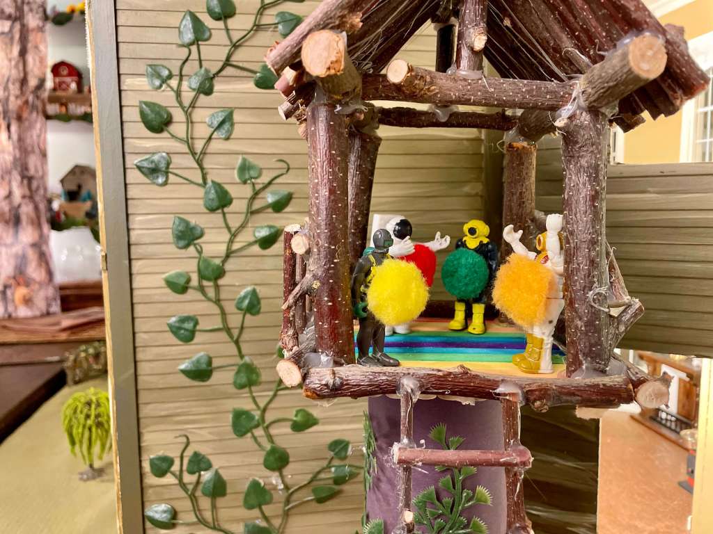 Small toys in a treehouse with circles of different colours on their stomachs