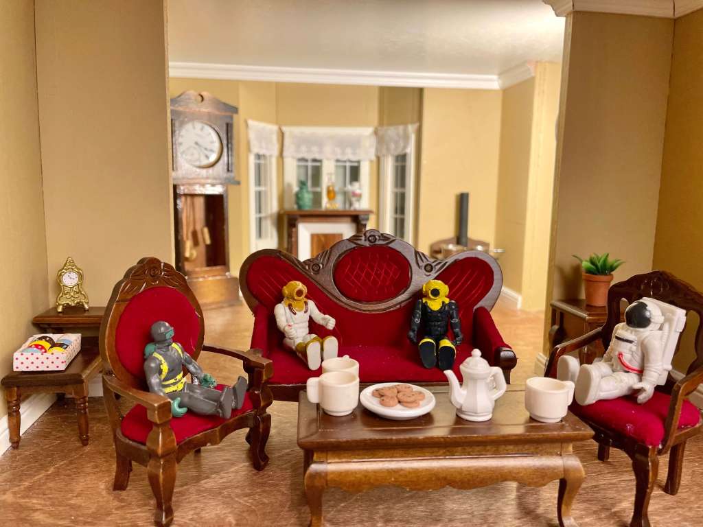 Group of small toys sitting around a table with tea and cookies
