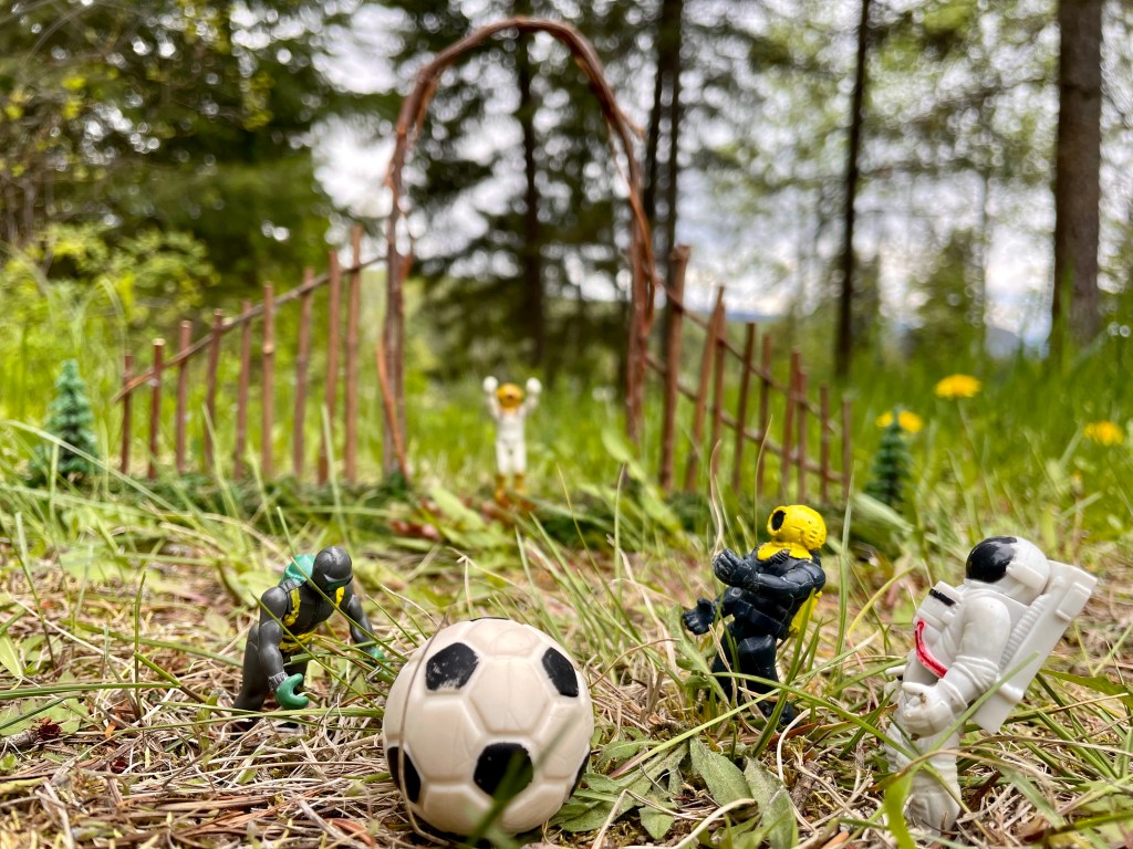 Small toys are playing soccer. One looks like it is tripping while two others are laughing