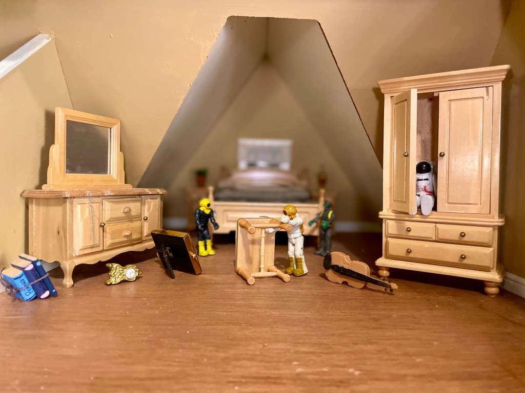 1 toy flipping furniture with books, a clock, a frame, and a violin on the ground. 2 toys behind and 1 hiding in a closet