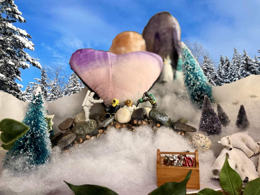 2 toys holding up a large heart with 2 toys sitting in front of it. Toy tools in front with polar bears in a snowy scene