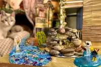 4 toys jumping into puddles with water splashing. A fountain in the middle with a tree, house, castle, and a cat in the back