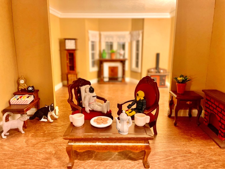 Two small toys sitting around a table with tea and cookies